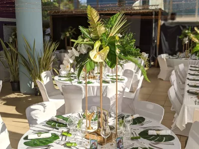 Grand centre de table exotique de mariage, composé d'anthuriums pâles, d'orchidées et d'une profusion de feuillages tropicaux dorés.
