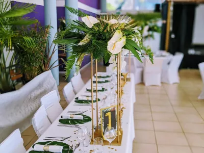 Centre de table de mariage exotique et moderne avec anthuriums, orchidées et feuillages tropicaux dorés et verts.