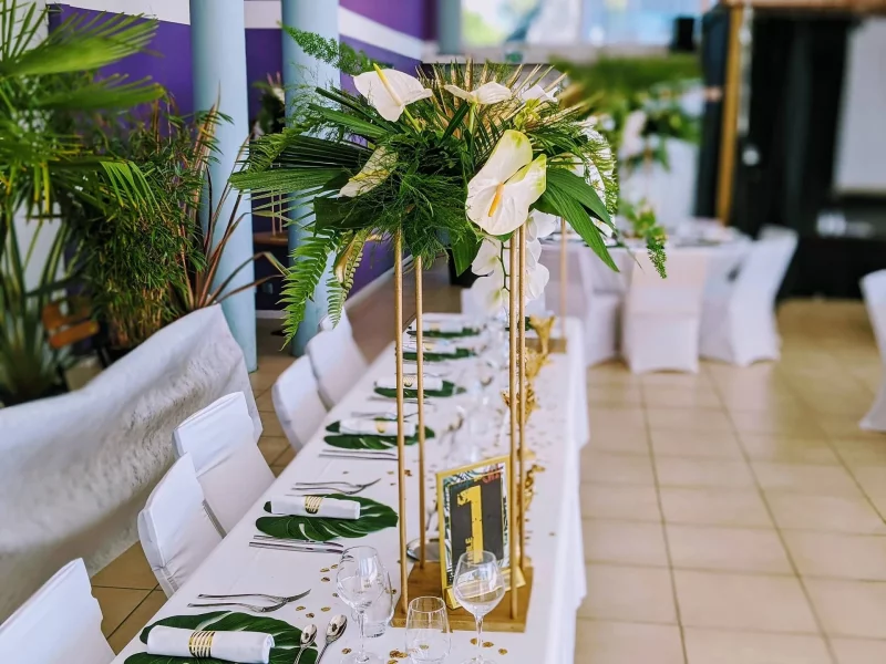 Centre de table de mariage exotique et moderne avec anthuriums, orchidées et feuillages tropicaux dorés et verts.