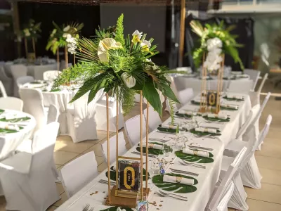 Centre de table de réception de mariage exotique, avec des anthuriums blancs et des orchidées, entourés de feuillages verts et dorés.