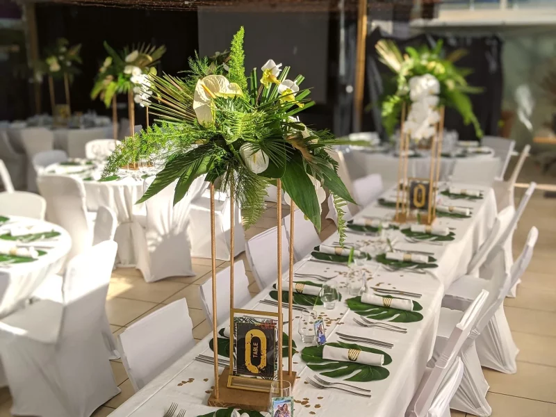 Centre de table de réception de mariage exotique, avec des anthuriums blancs et des orchidées, entourés de feuillages verts et dorés.