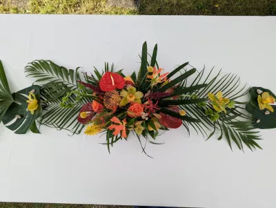 Grand centre de table exotique avec anthurium, roses orange, orchidées et feuilles de palmier pour table de mariage.
