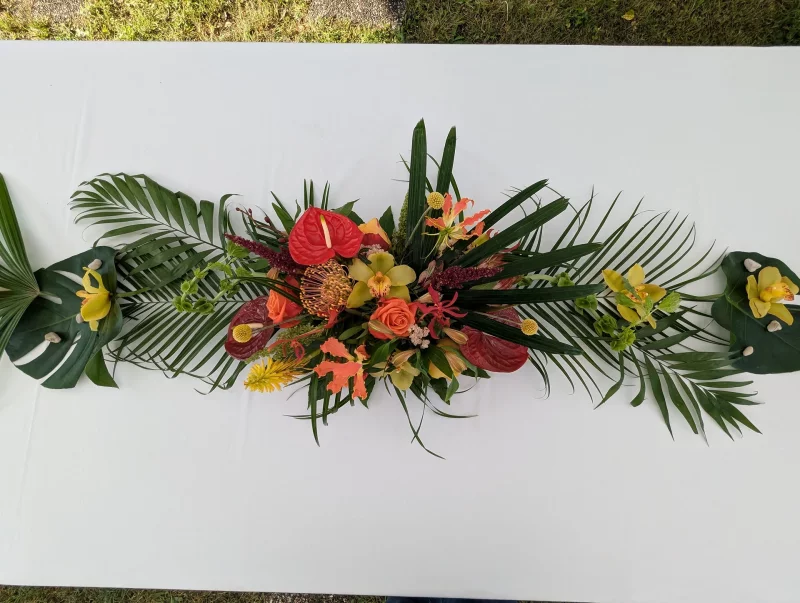 Grand exotic table centrepiece with anthurium, orange roses, orchids and palm leaves for a wedding table.