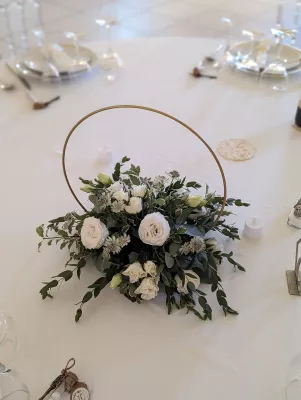 Centre de table mariage bohème moderne avec roses blanches, eucalyptus, et cercle doré, ambiance élégante et lumineuse.