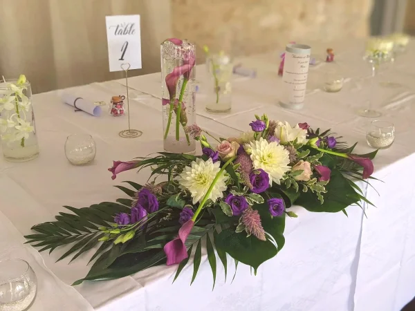 Centre de table allongé mariage moderne, dahlias crème, callas violets, lisianthus, feuillage exotique au Domaine De Larchey.