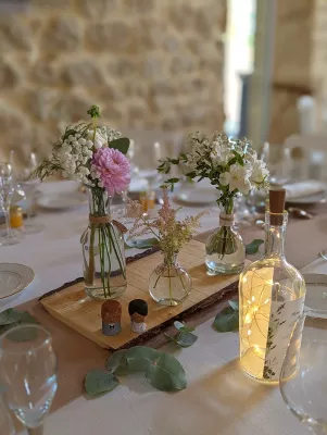 Centre de table champêtre avec dahlias roses, gypsophile et astilbe dans divers petits vases sur une planche en bois.