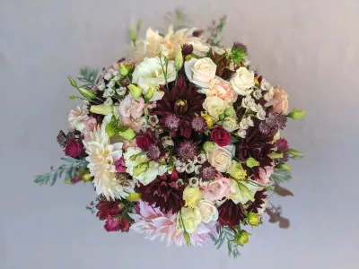 Centre de table rond et opulent pour mariage champetre, avec dahlias creme et bordeaux, roses, oeillets et feuillage.