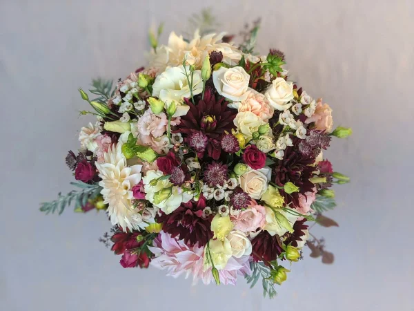 Centre de table rond et opulent pour mariage champetre, avec dahlias creme et bordeaux, roses, oeillets et feuillage.