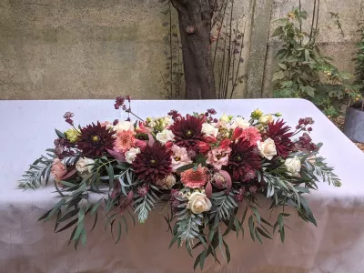 Grand centre de table champetre pour reception de mariage, avec dahlias bordeaux, roses creme, oeillets peche et feuillage vert.