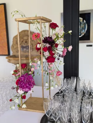 Centre de table classique avec dahlias bordeaux, roses rouges et feuillage vert sur structure dorée, pour un mariage.