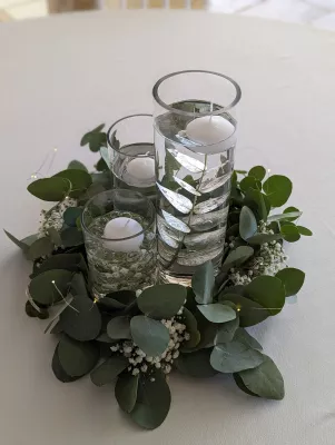 Centre de table champêtre avec eucalyptus, gypsophile et bougies flottantes dans des verres cylindriques.