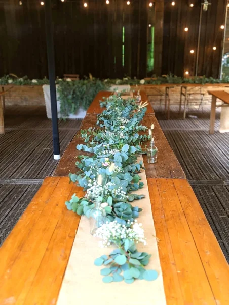 Long centre de table champêtre avec guirlande d'eucalyptus et gypsophile sur table en bois, mariage Airial de Pernaud.