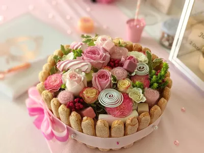 Centre de table original en forme de gâteau avec roses, carnations, baies rouges et ruban rose, style classique pour mariage.