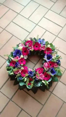 Centre de table classique pour mariage avec des gerberas fuchsia, des anémones bleues et du feuillage vert, ambiance vibrante.