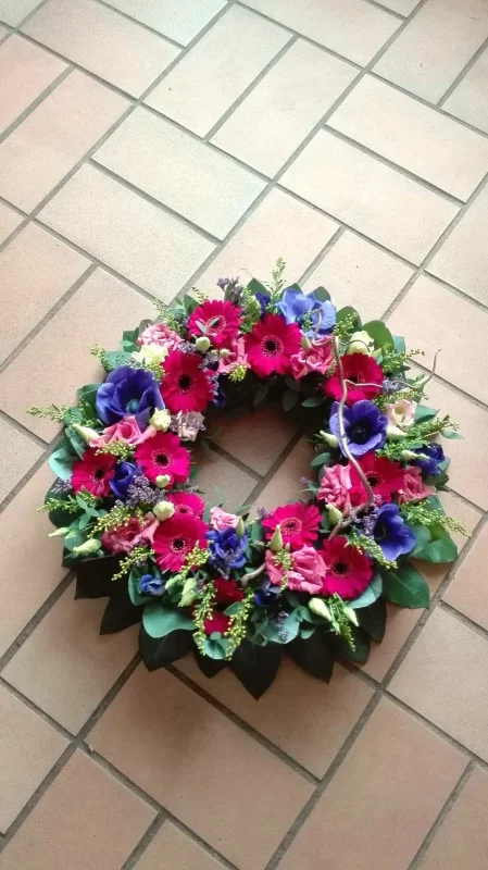 Centre de table classique pour mariage avec des gerberas fuchsia, des anémones bleues et du feuillage vert, ambiance vibrante.