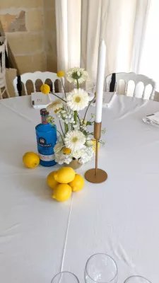 Décoration de centre de table de mariage avec gerberas blancs, craspedias jaunes, et une bouteille bleue style limoncello