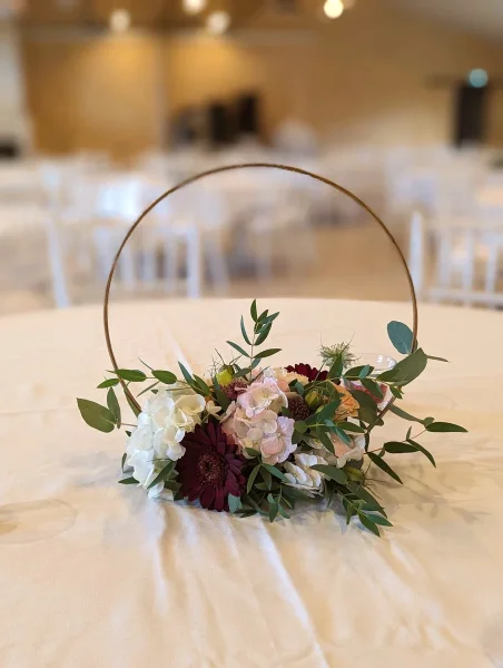 Centre de table bohème avec gerbera bordeaux, hortensia blanc et rose, et feuillage eucalyptus pour mariage estival.