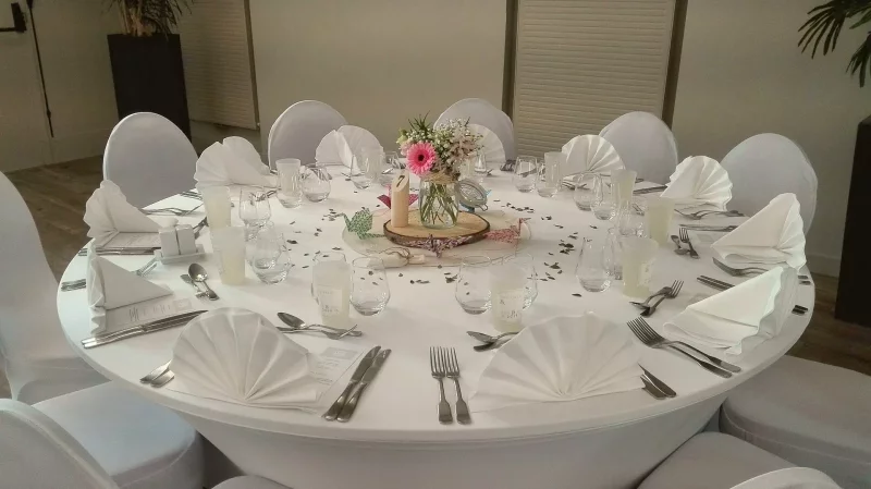 Centre de table de mariage champêtre avec un gérbera rose, des marguerites et des petites roses dans un pot en verre sur un rondin de bois.
