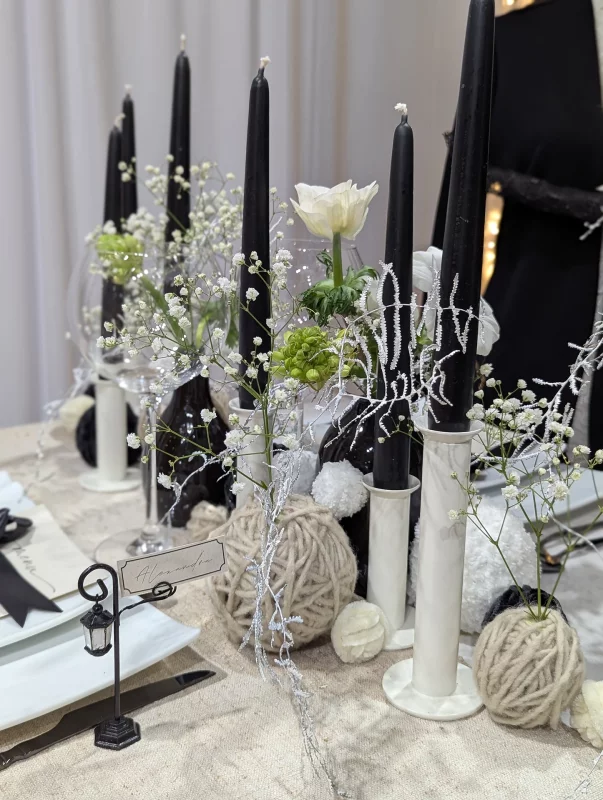 Centre de table minimaliste avec bougies noires, gypsophile, rose blanche et elements decoratifs en fil.