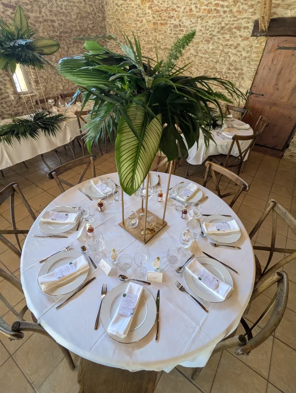 A grand, exotic table centrepiece on a golden stand, with a lush arrangement of monstera and palm leaves.