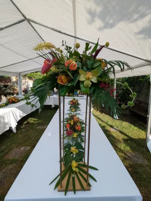 Centre de table exotique haut avec anthurium, roses orange, orchidées cymbidium et feuillage tropical pour un mariage.