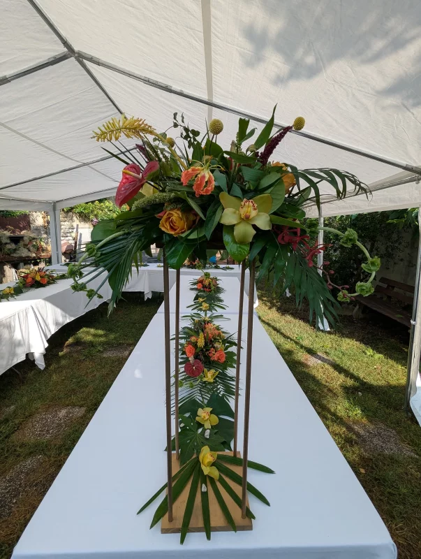 Elevated exotic table centrepiece with anthurium, orange roses, cymbidium orchids and tropical foliage for a wedding.