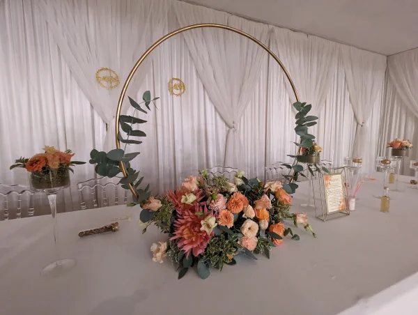 Grande composition florale bohème pour table d'honneur avec roses pêche, dahlias corail, eucalyptus et cercle doré.