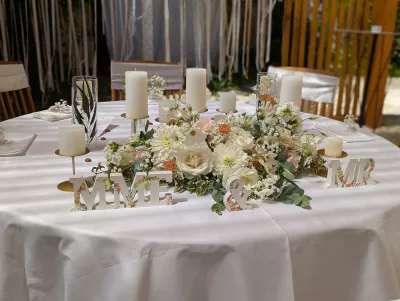 Composition florale de table d'honneur pour mariage avec roses blanches, dahlias, gypsophile, alstroemerias roses et feuillage verdoyant.