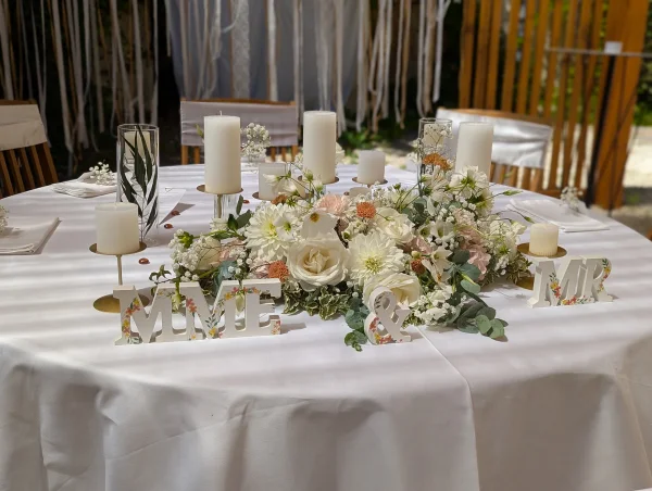 Composition florale de table d'honneur pour mariage avec roses blanches, dahlias, gypsophile, alstroemerias roses et feuillage verdoyant.