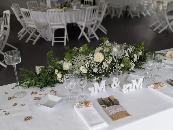 Long centre de table d'honneur champêtre avec roses, gypsophile et feuillage vert, pour mariage.