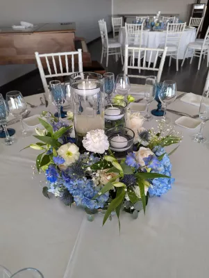 Centre de table mariage champêtre chic avec hortensias bleus, roses blanches et œillets pour le mariage de Salomé.