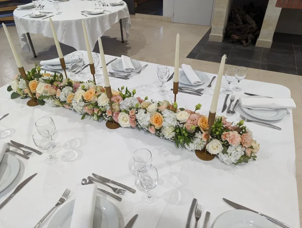 Centre de table long et fleuri avec hydrangeas, roses et carnations dans les tons pastel pour un mariage.