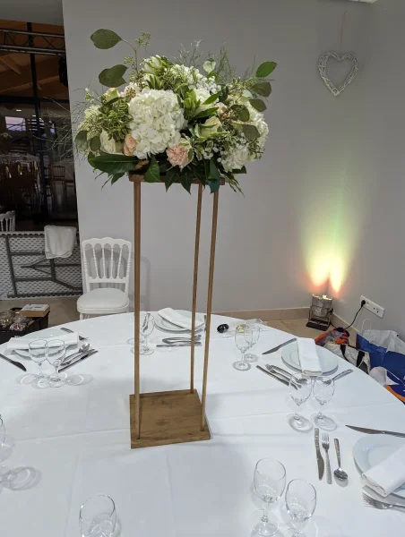 Centre de table haut sur support en bois avec hydrangeas blancs, roses peches et feuillage, mariage classique.