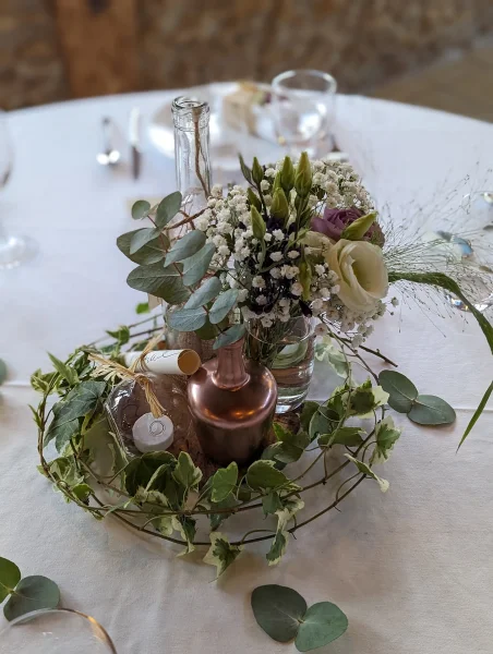 Centre de table champêtre avec lisianthus blancs et violets, gypsophile et lierre, dans des contenants variés.