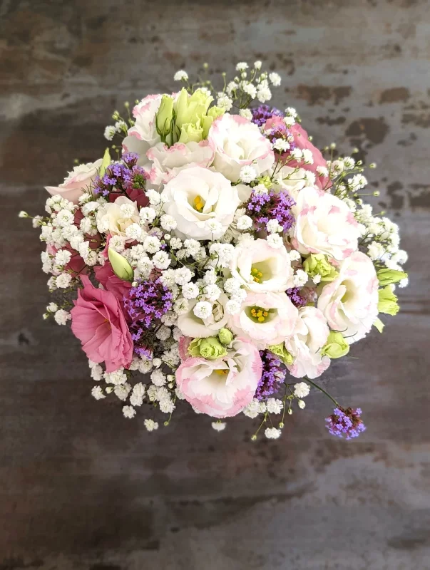 Centre de table classique pour mariage d'été, avec lisianthus blancs et roses, gypsophile délicate et accents violets, créant une ambiance douce et romantique.