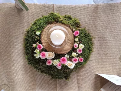 Centre de table champêtre circulaire avec mousse, roses roses et crème, et bougie blanche pour mariage.