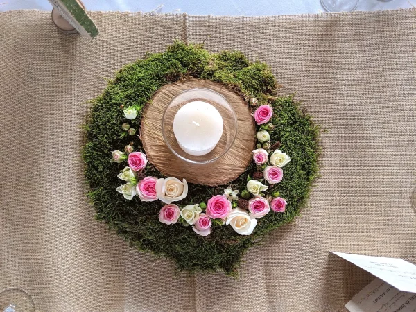 Centre de table champêtre circulaire avec mousse, roses roses et crème, et bougie blanche pour mariage.