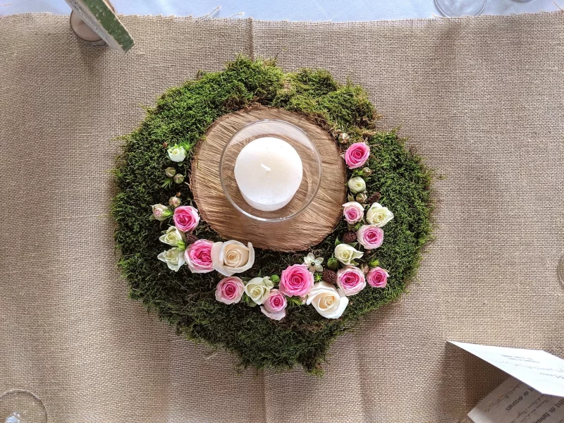 Centre de table champêtre circulaire avec mousse, roses roses et crème, et bougie blanche pour mariage.