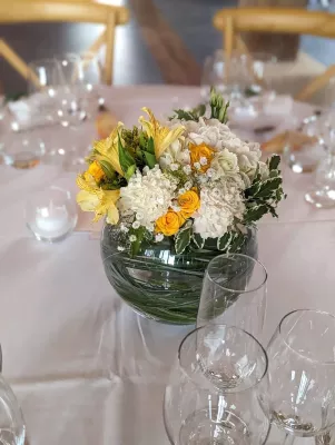 Centre de table champêtre floral avec œillets blancs, alstroemerias jaunes et feuillage panaché dans un vase en verre.