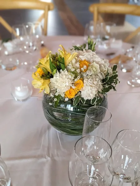 Centre de table champêtre floral avec œillets blancs, alstroemerias jaunes et feuillage panaché dans un vase en verre.