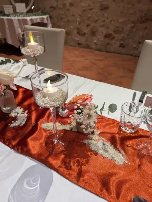 Detail of a sophisticated rustic centrepiece with orange carnations, roses, and foliage for a wedding.