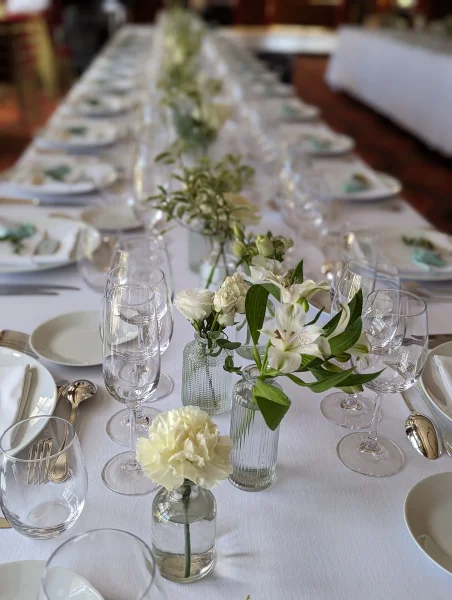 Centres de table de mariage minimalistes avec œillet blanc, rose et alstroemeria dans de petits vases pour un dîner élégant.