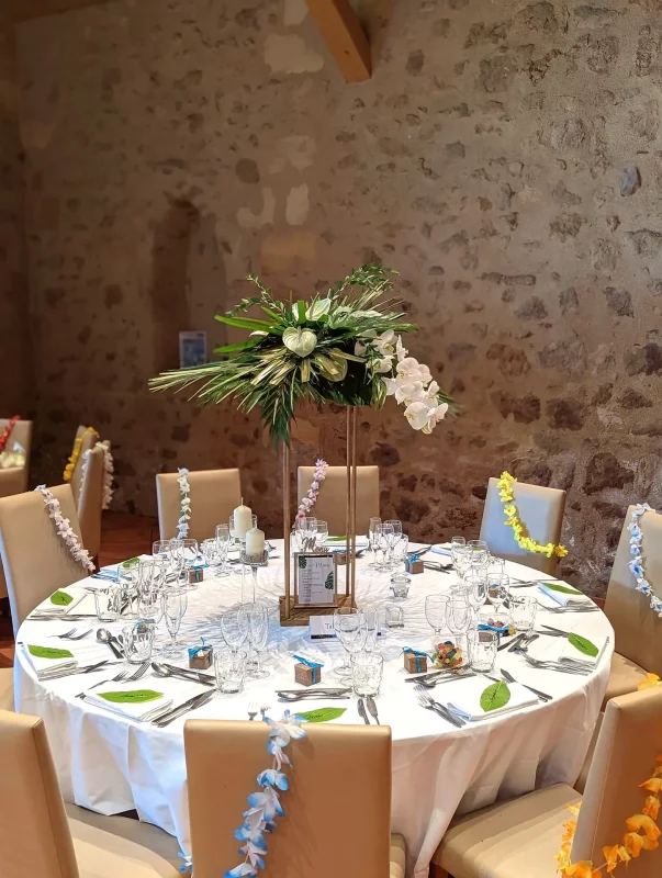 Exotic table centrepiece for Girard's wedding, featuring orchids, anthuriums, and tropical foliage on golden columns in Pessec.