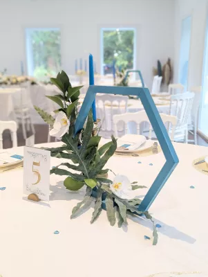 Sophisticated country wedding table centrepiece with white orchids, foliage, and blue hexagonal structure.