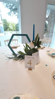 Minimalist table centrepiece with white orchid, green foliage, and blue candle on a white table.