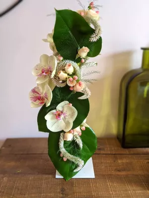 Centre de table mariage exotique moderne avec orchidées blanches et roses pêche, agrémenté de feuillage vert luxuriant.