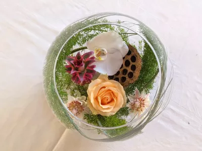 Vue plongeante d'un centre de table exotique avec orchidée blanche, rose pêche, guzmania et lotus séché