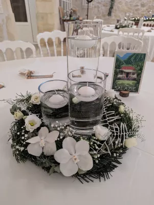 Décoration de table de mariage classique avec orchidées et roses blanches, feuillage hivernal et bougies flottantes.