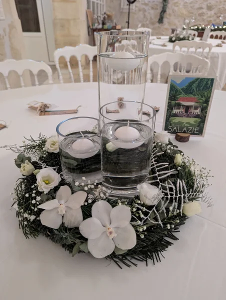 Décoration de table de mariage classique avec orchidées et roses blanches, feuillage hivernal et bougies flottantes.