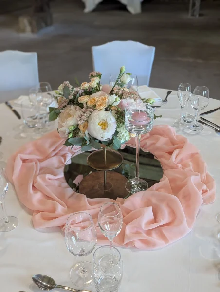 Centre de table de mariage classique avec pivoines, roses pêche et eucalyptus, sur un support doré et un miroir.